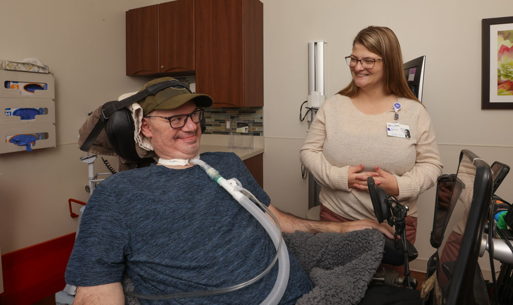 A man with a trach and his caregiver smiling at each other.
