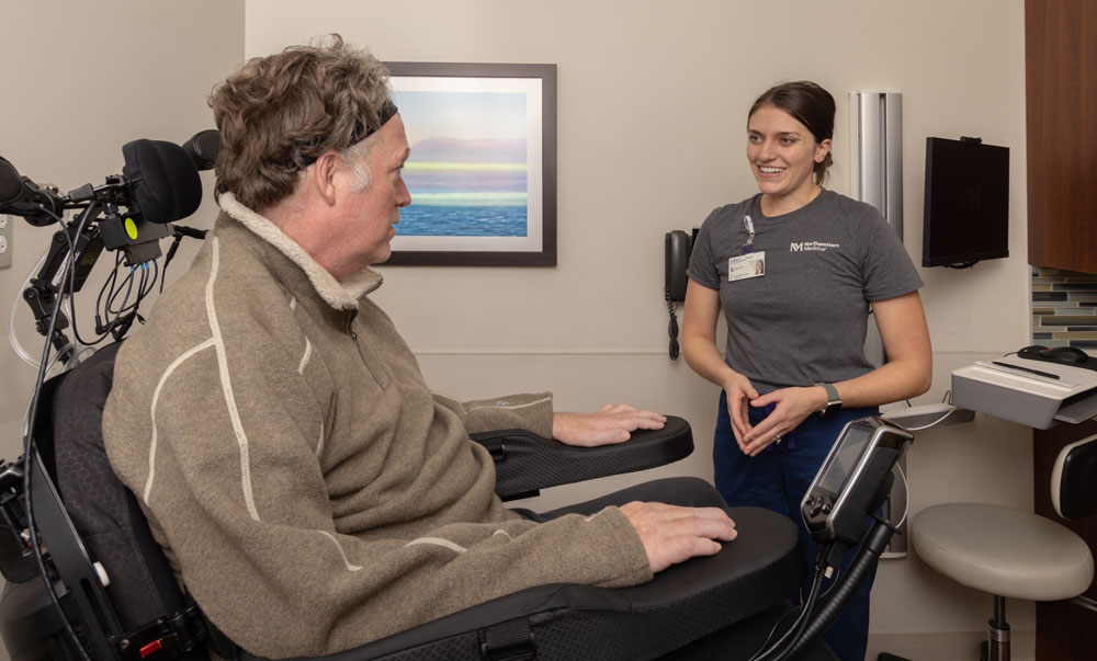 A man in an electric wheelchair talks with a member of his care team.