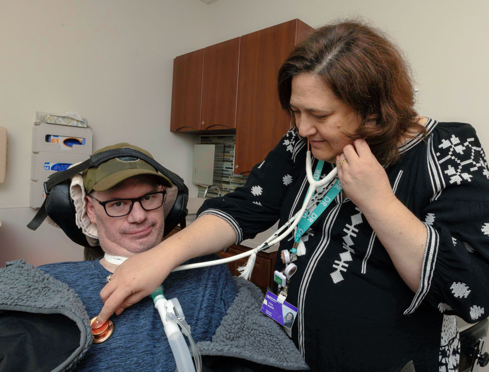 A physician using a stethoscope on a man with a trach.