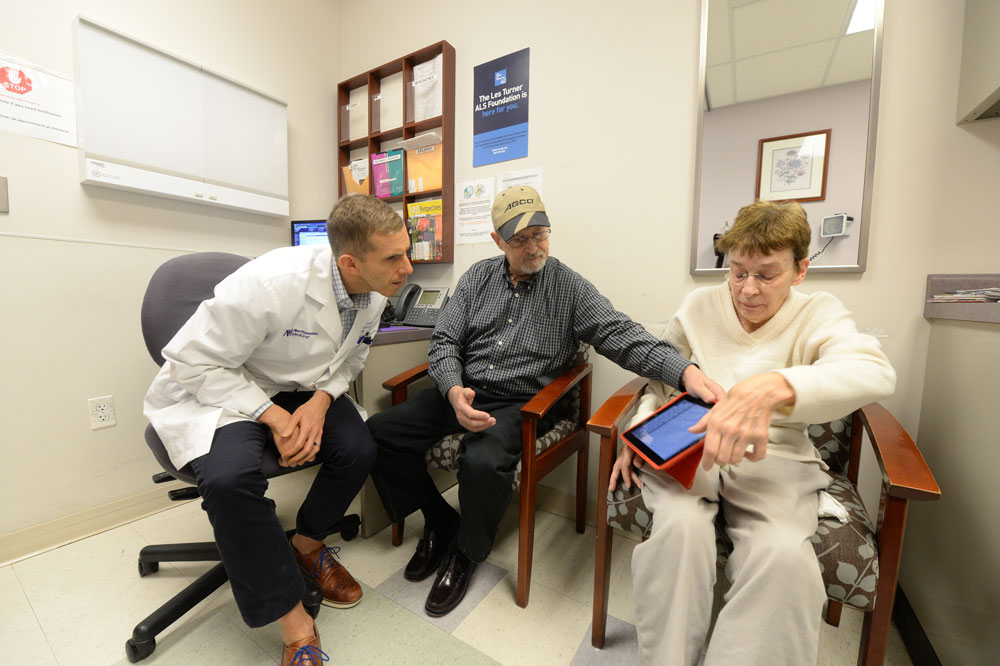 A woman using augmentative and alternative communication, or AAC, to communicate with her doctor. Her caregiver is helping her select words on a tablet.